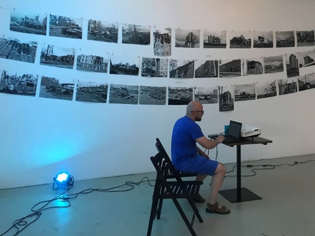 Der Hobbyfotograf Marcin Kròl sitzt am Computer. Hinter ihm sind einige seiner Fotos an der Wand.