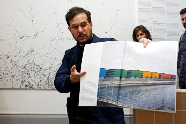 Mann präsentiert in einem Museum eine Bild mit farbigen Gebäuden ©Hans H. Münchhalfen