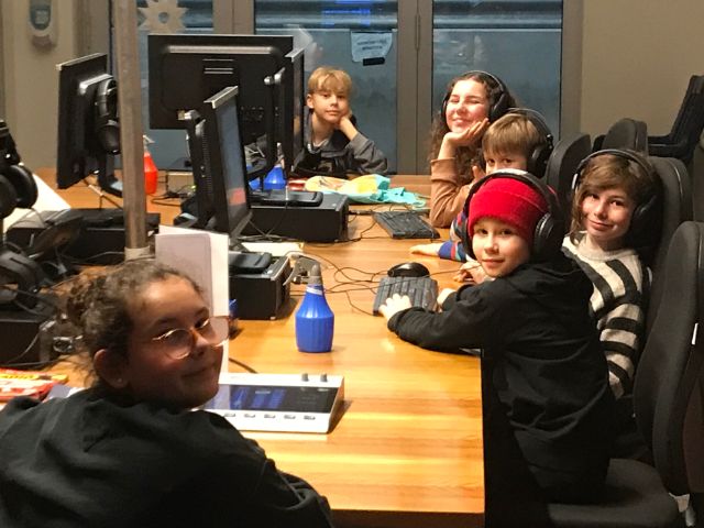Eine Kindergruppe arbeitet an grossem Tisch mit Computern und Kopfhörern